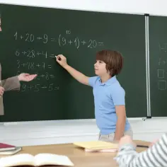 Nauczycielka pomaga uczniowi rozwiązać zadanie z matematyki przy tablicy. Czy uczeń może poprawić każdą ocenę? Tak, pracą i zaangażowaniem.
