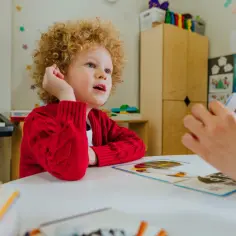 Chłopiec z kręconymi włosami, uczeń z autyzmem, uczy się z kart obrazkowych.