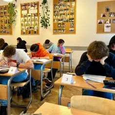 Uczniowie piszą egzamin. Na ścianach wiszą zdjęcia. Gdzie znaleźć numer dopuszczenia programu nauczania?