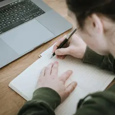 Osoba pisze w notatniku obok laptopa. Zastanawia się, czy opinia z niepublicznej poradni jest ważna.