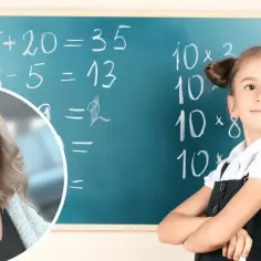 Uśmiechnięta dziewczynka z kucykami stoi przy tablicy z zadaniami matematycznymi. Nauczycielka w okularach wspiera ją w pokonywaniu problemów z matematyką.