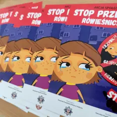 Plakaty z hasłem "STOP przemocy rówieśniczej" pokazują smutną dziewczynkę i złośliwe karykatury dzieci.