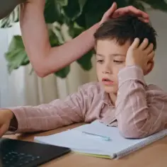 Zrezygnowany chłopiec przy laptopie, ręka na głowie. Rodzic próbuje go pocieszyć. Dziecko nie chce się uczyć, potrzebna pomoc psychologa.