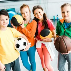 Czterech uśmiechniętych młodych ludzi z piłkami, gotowych do zabawy. Sport to radość dla każdego, niezależnie od niepełnosprawności ruchowej.