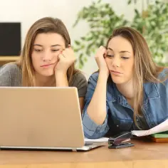 Dwie znudzone nastolatki przy laptopie, zmęczone nauką zdalną.