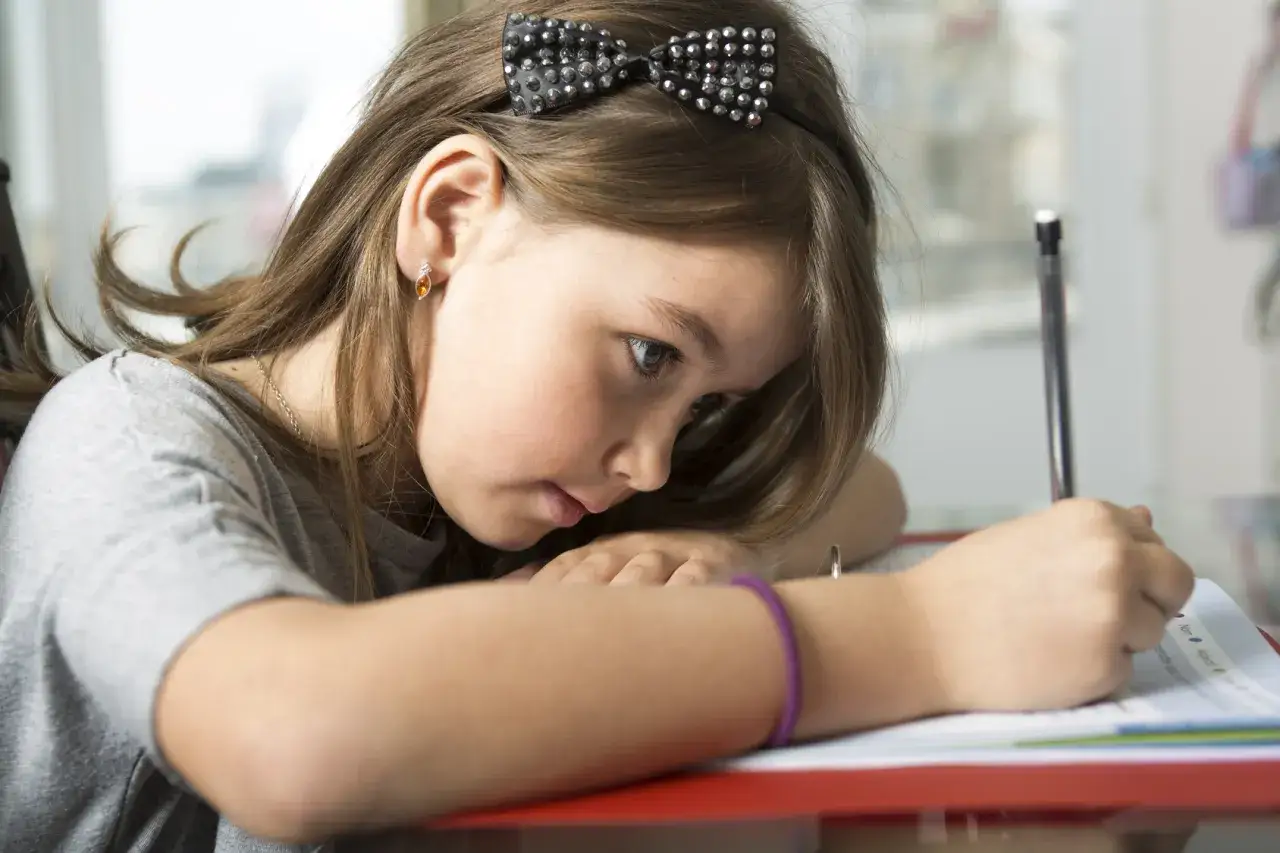 Dziewczynka z kokardką na głowie zmagająca się z zadaniem domowym. Czy dysleksja to choroba?