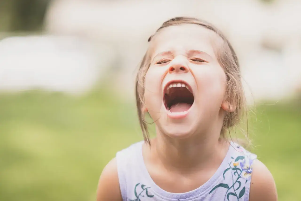 Mała dziewczynka krzyczy z otwartymi ustami, pokazując zęby. Wygląda na to, że jest dzieckiem odpornym psychicznie, które wyraża swoje emocje.