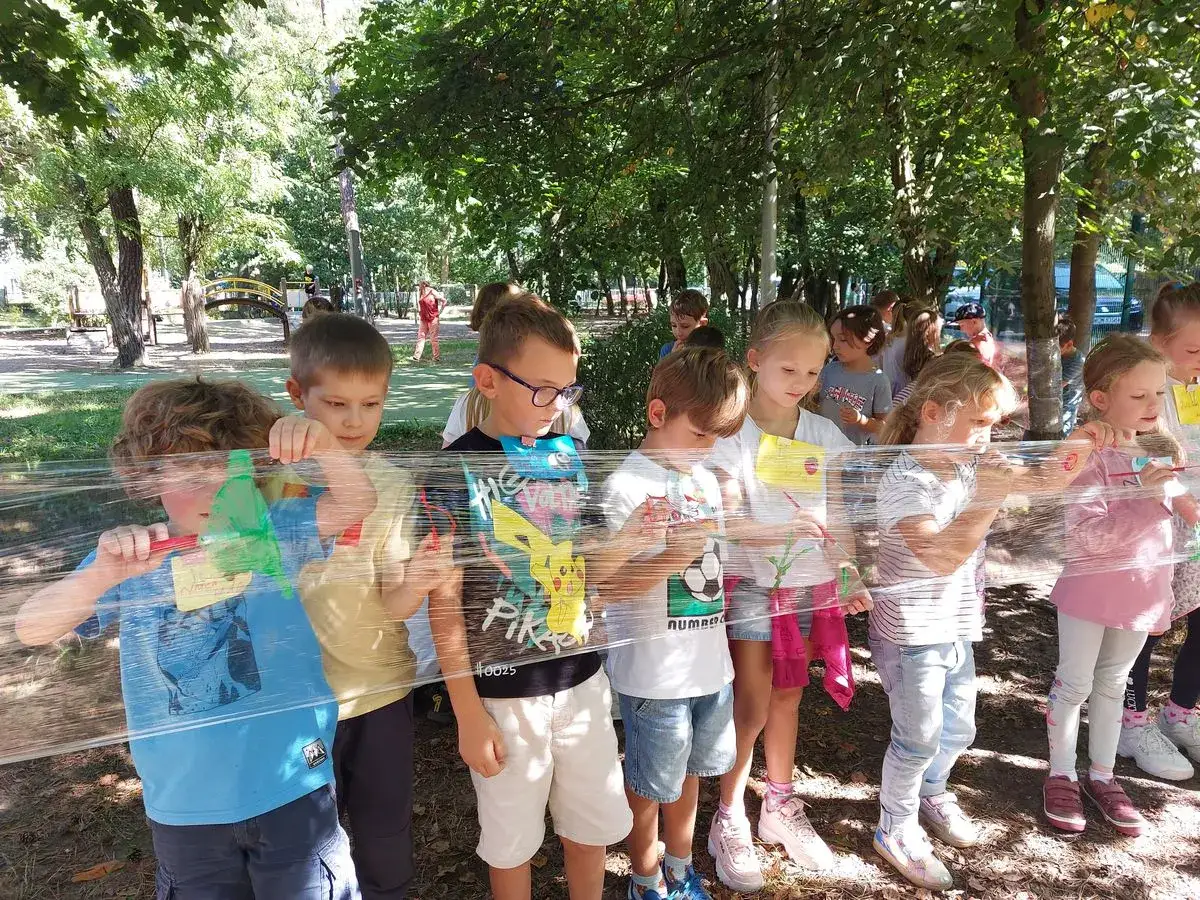 Dzieci biorą udział w edukacji outdoorowej, malując na folii rozpiętej między drzewami.