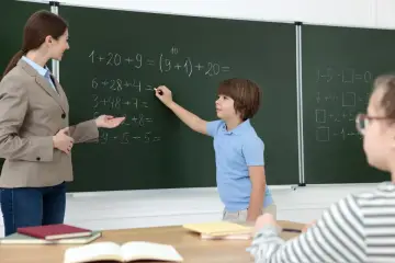Nauczycielka pomaga uczniowi rozwiązać zadanie z matematyki przy tablicy. Czy uczeń może poprawić każdą ocenę? Tak, pracą i zaangażowaniem.