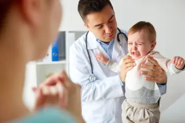 Lekarz uspokaja płaczące dziecko, które przechodzi skoki rozwojowe. Mama patrzy z troską.